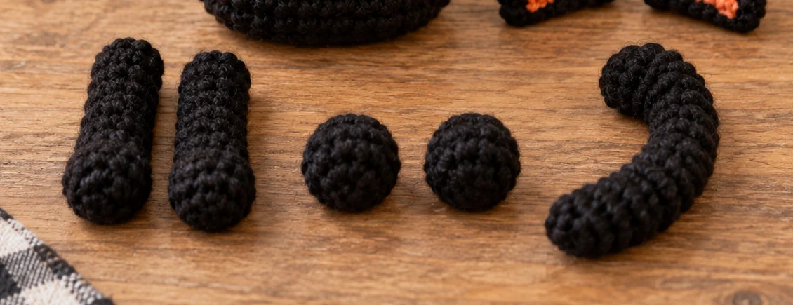 Crochet black cat paws and curved tail pieces before assembly