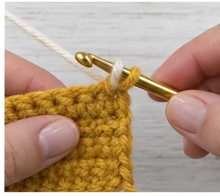 Cream yarn pulled through two mustard loops on a crochet hook