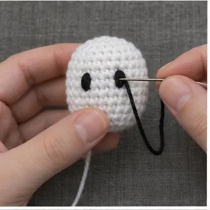 Embroidering black eyes on the white crochet ghost