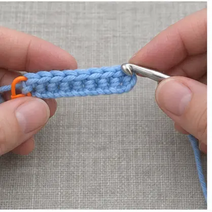 Crochet hook entering the marked last stitch of a blue row